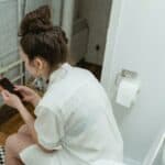 picture of woman sitting on a toilet scrolling on her phone
